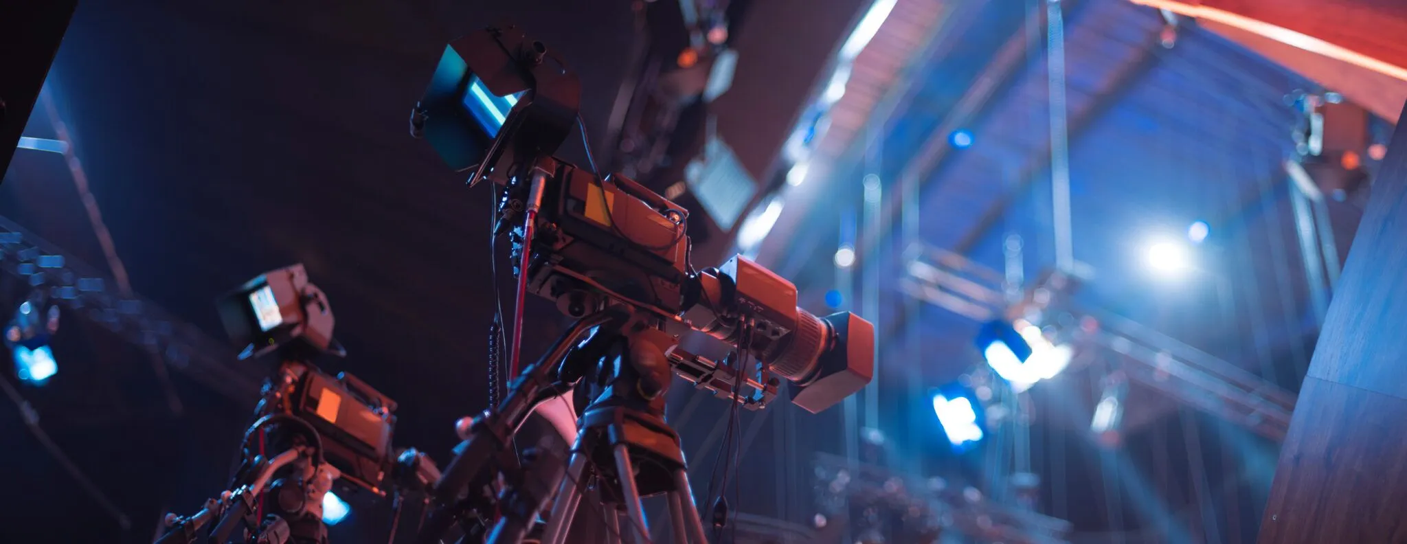 Multiple professional cameras set up on tripods, capturing a live event under stage lighting.