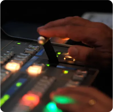 Close-up of a hand operating a professional broadcasting control panel with illuminated buttons and switches, showcasing competitive broadcasting packages.
