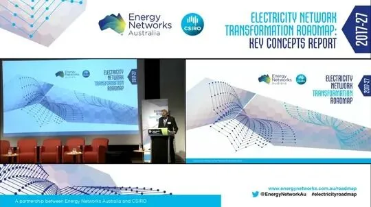 Speaker presenting at an industry conference with a detailed presentation slide in the background, highlighting energy network transformation roadmap.
